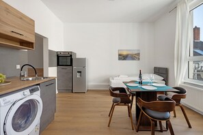 A compact kitchen with a washing machine, a dining area with a table and chairs, and a window with a view. - 2-Room Apartment 3-3 with Wi-Fi (Lübeck)