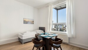 Een slaapkamer met een bed, een eettafel met stoelen, een raam met gordijnen en een schilderij aan de muur.