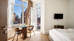 A bedroom with a bed, a TV, a desk with chairs, and a window with curtains. - 2-room apartment 2-2 with balcony and Wi-Fi (Lübeck)