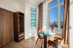 Una stanza con un armadio in legno, un tavolo con sedie, una finestra con tende e vista sugli edifici esterni.
