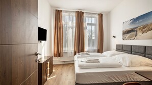A bedroom with a bed, a TV, a window with curtains, and a painting on the wall. - 2-room apartment 2-2 with balcony and Wi-Fi (Lübeck)