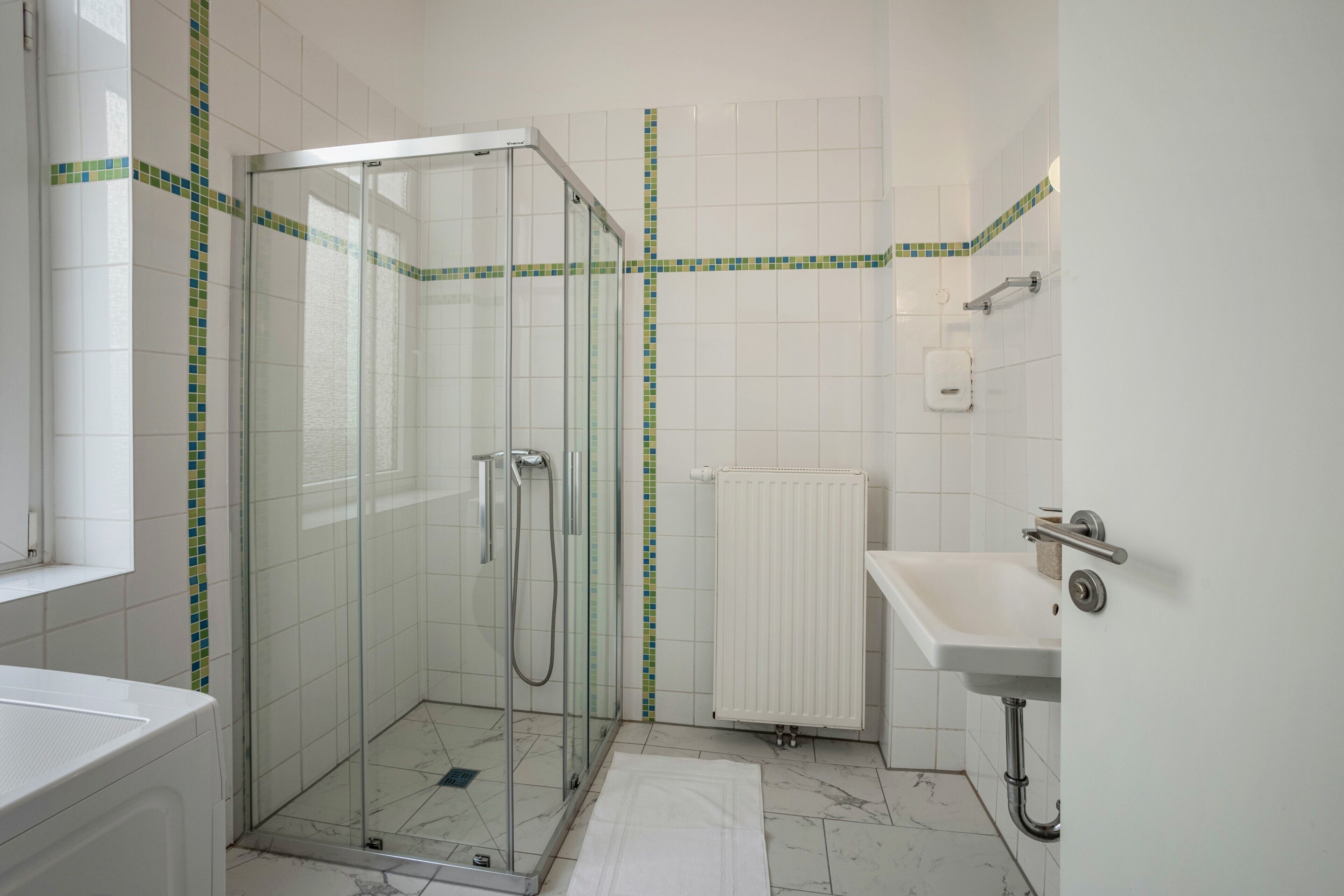 A bathroom with a glass-enclosed shower, a white sink, a radiator, and a tiled floor.