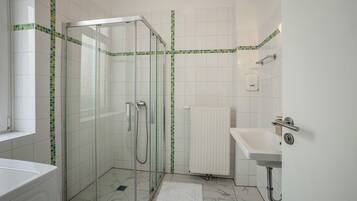 A bathroom with a glass-enclosed shower, a white sink, a radiator, and a tiled floor.