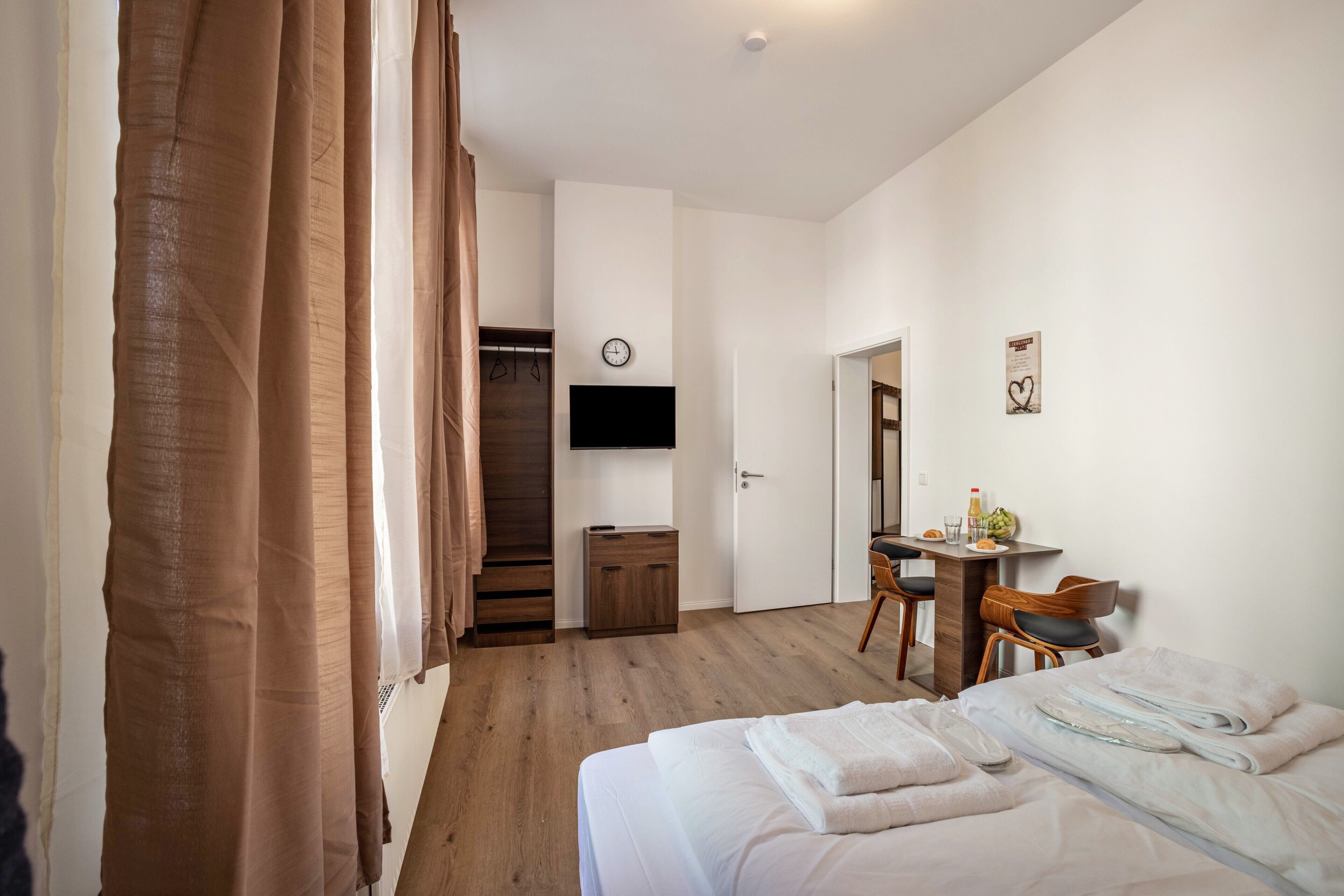 Ein Hotelzimmer mit Bett, Schreibtisch, Sessel, Fernseher und einer Wanduhr.