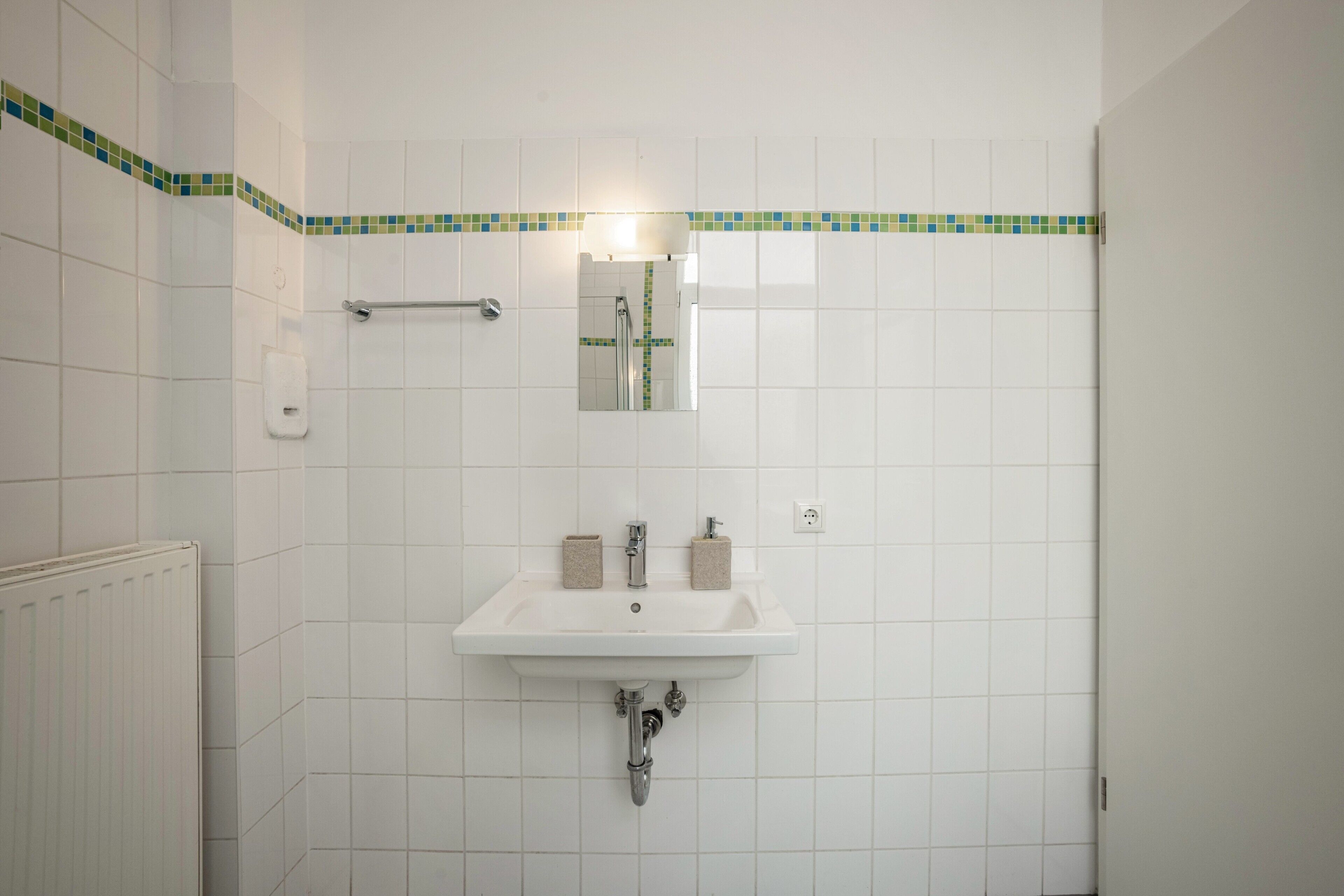 A bathroom with a white sink, mirror, and tiled walls.
