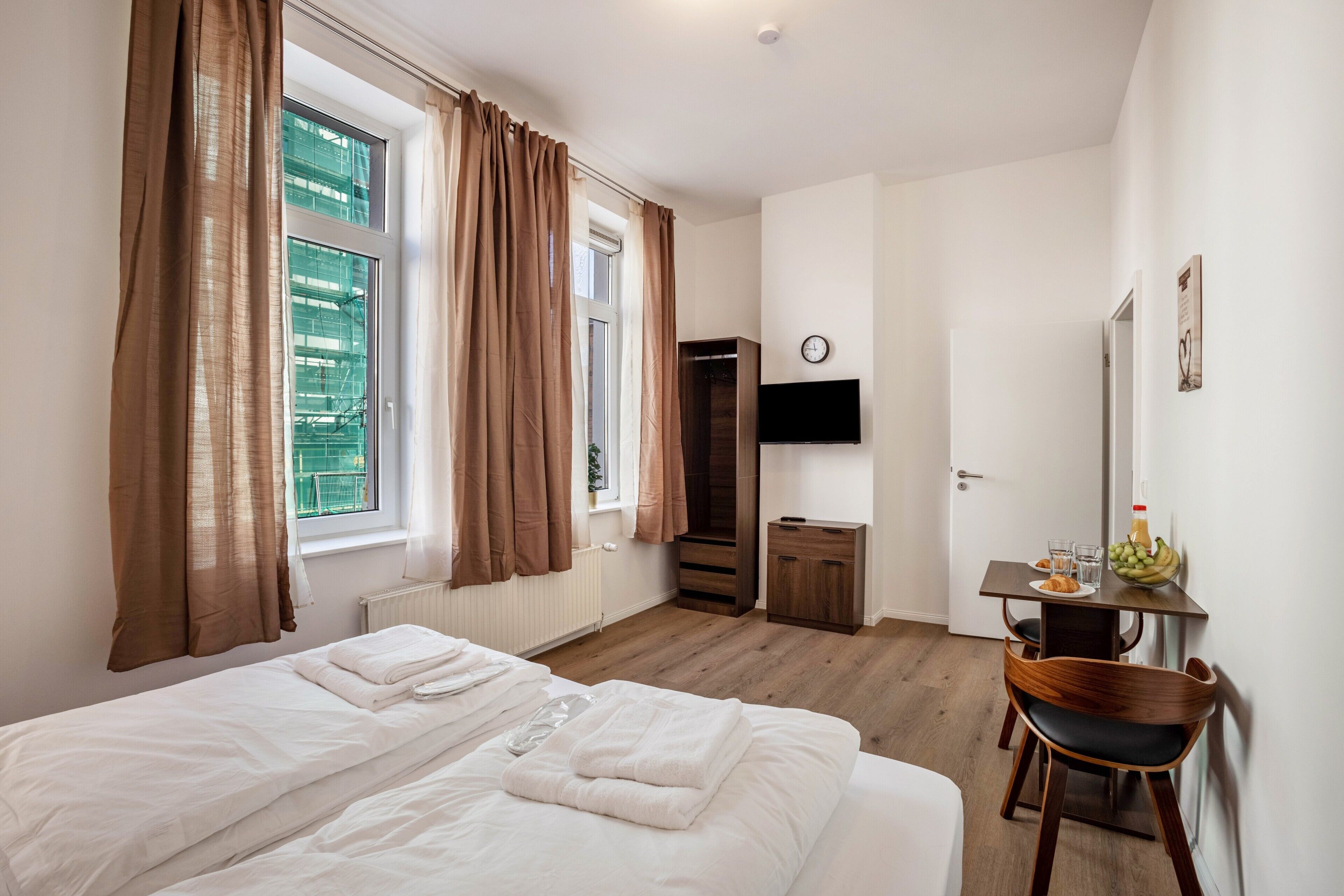 Une chambre d’hôtel équipée d’un lit, d’un bureau, d’une chaise, d’une télévision et d’une fenêtre avec des rideaux.