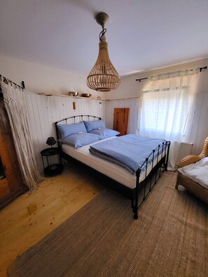 Une chambre à coucher avec un lit, une table de chevet, un luminaire suspendu et une fenêtre avec des rideaux.