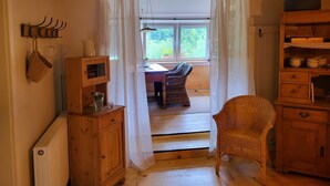 Een houten kamer met een rieten stoel, een houten kast en een raam met uitzicht op groen.