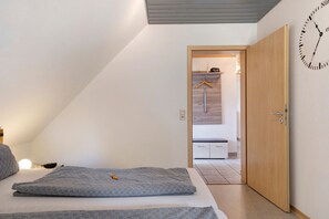 Une chambre à coucher avec un lit, une horloge au mur et une porte donnant sur une salle de bain.