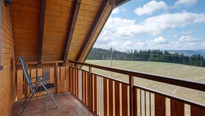 Ein Holzbalkon mit Blick auf ein Wiesfeld und Bäume.