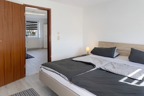 Ein Schlafzimmer mit Bett, Nachttisch, Lampe und Blick aus dem Fenster.