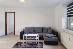 Ein modernes Wohnzimmer mit einem Ecksofa, einem Glastisch und Blick durch ein Fenster.