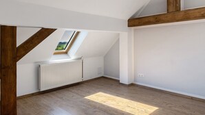 A room with a sloped ceiling, wooden beams, a skylight, a radiator, and a wooden floor. - Holiday Home 'Ferienhaus' with Private Terrace, Private Garden and Wi-Fi (Zernitz-Lohm)