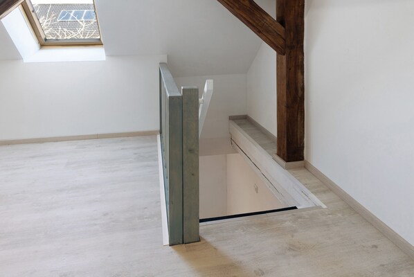Un escalier avec une rampe en bois, des murs blancs et une lucarne.