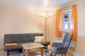 Ett vardagsrum med en grå soffa, en blå fåtölj, ett träbord och en golvlampa.
