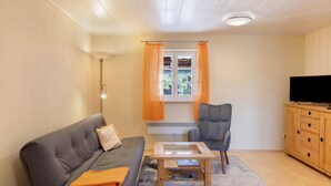 A living room with a sofa, armchair, coffee table, TV, and wooden cabinet. - Studio '30 sqm' with Wi-Fi in Historic Four-Sided Farmhouse (Friedewald)