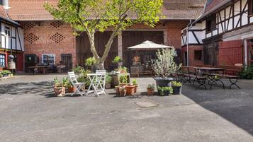A courtyard with a tree, potted plants, outdoor furniture, and a building with exposed timber framing.