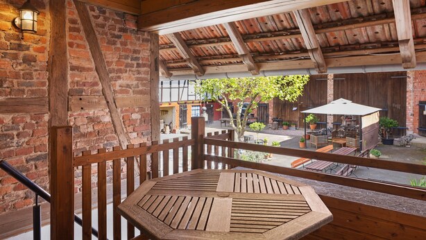 A wooden deck with a table and chairs, a brick wall, and a wooden ceiling. - Studio '30 sqm' with Wi-Fi in Historic Four-Sided Farmhouse (Friedewald)