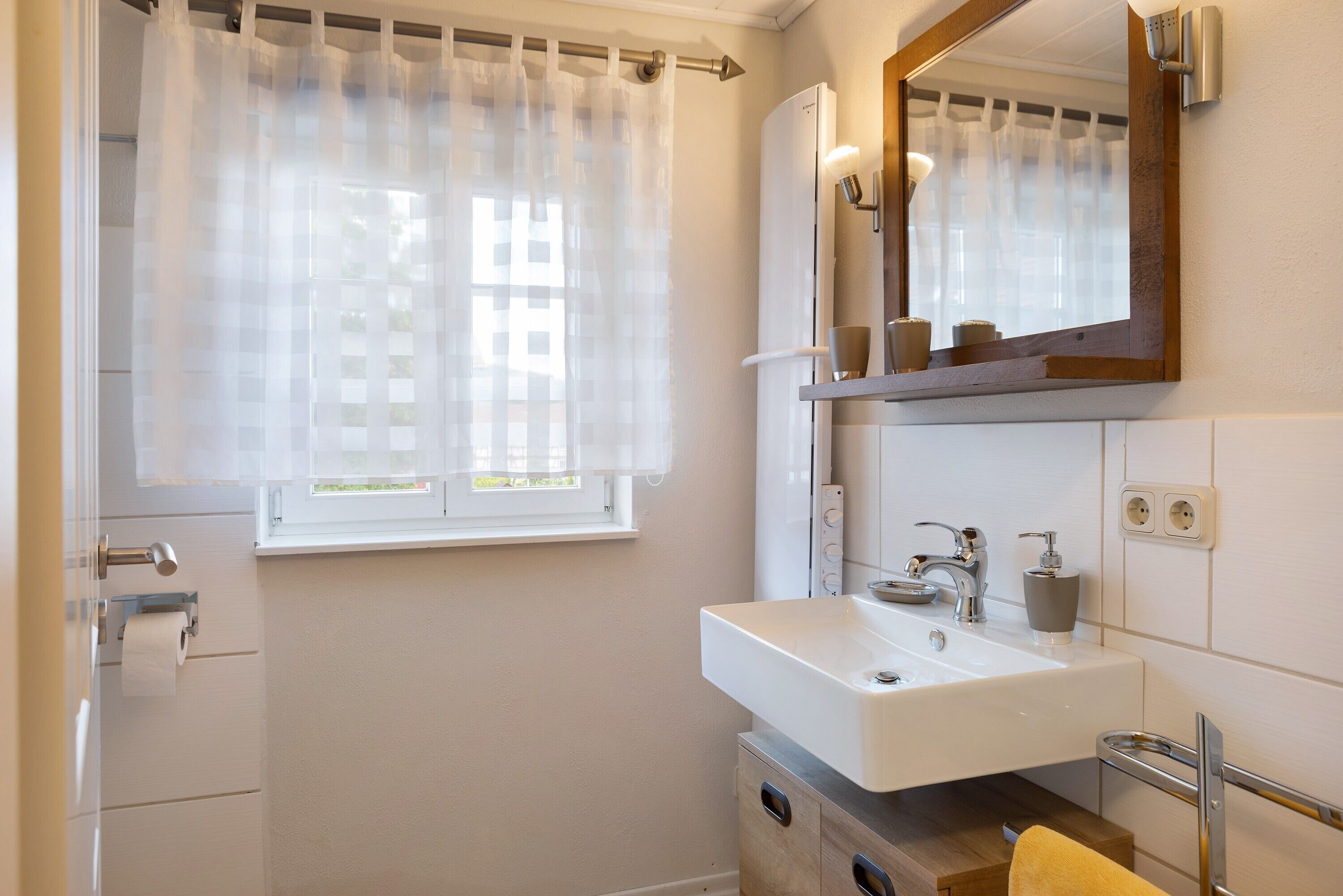 A bathroom with a white sink, mirror, and window with a curtain.