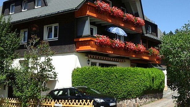 A two-story building with a balcony on the second floor, a car parked in front, and a hedge in the background. - Apartment '3' with Mountain View, Shared Garden and Wi-Fi (Hinterzarten)
