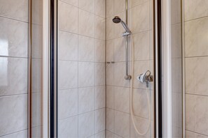 A corner shower with a handheld showerhead and a wall-mounted faucet.
