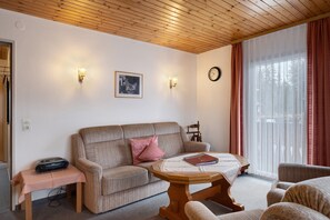 A living room with a sofa, a coffee table, a clock, and a window with curtains. - Apartment '3' with Mountain View, Shared Garden and Wi-Fi (Hinterzarten)