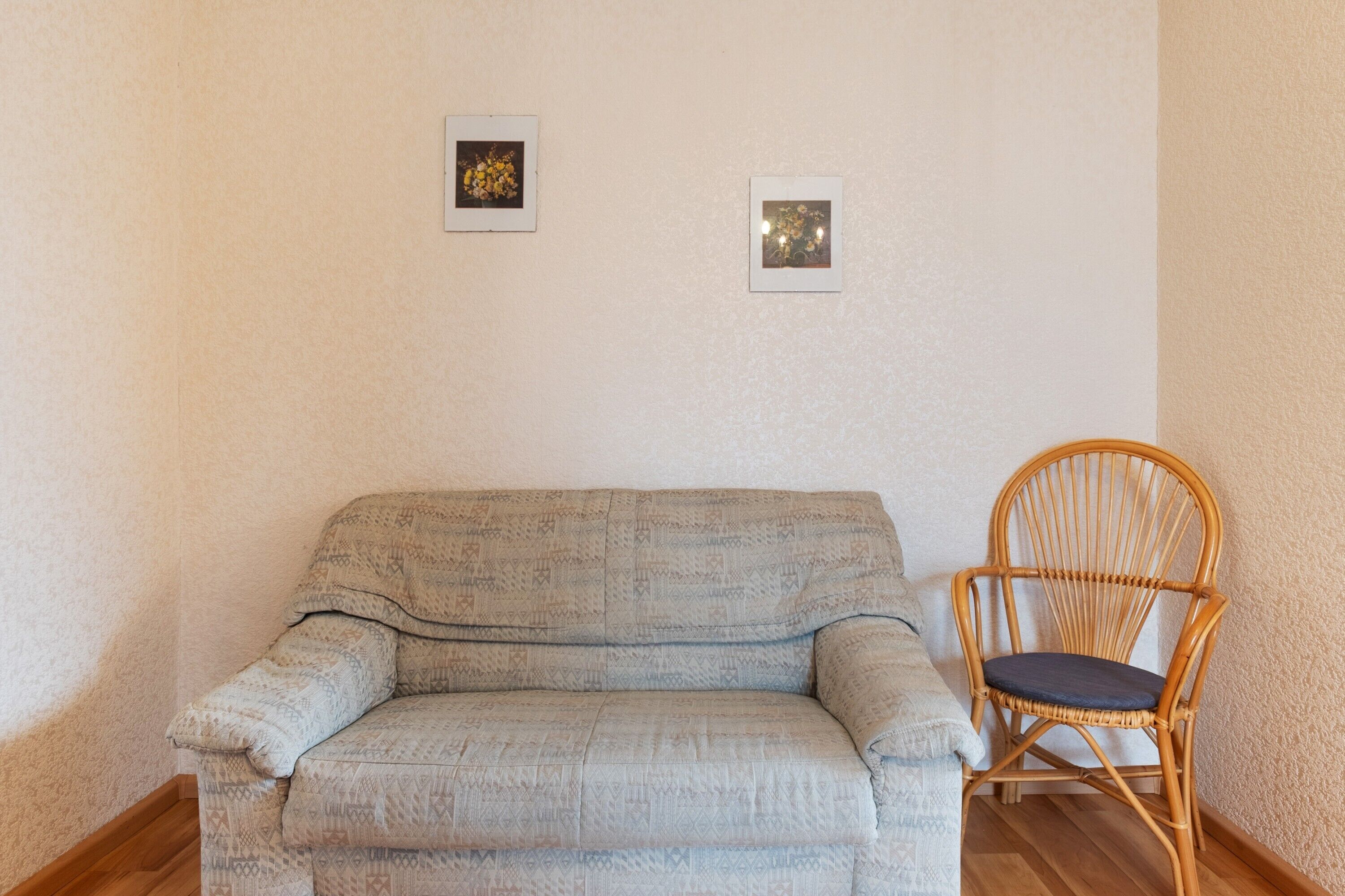 Une pièce avec un canapé à motifs, un fauteuil en osier et deux tableaux encadrés accrochés au mur.