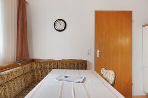 Een kamer met een bed, een houten deur, een klok aan de muur en een raam met gordijnen.