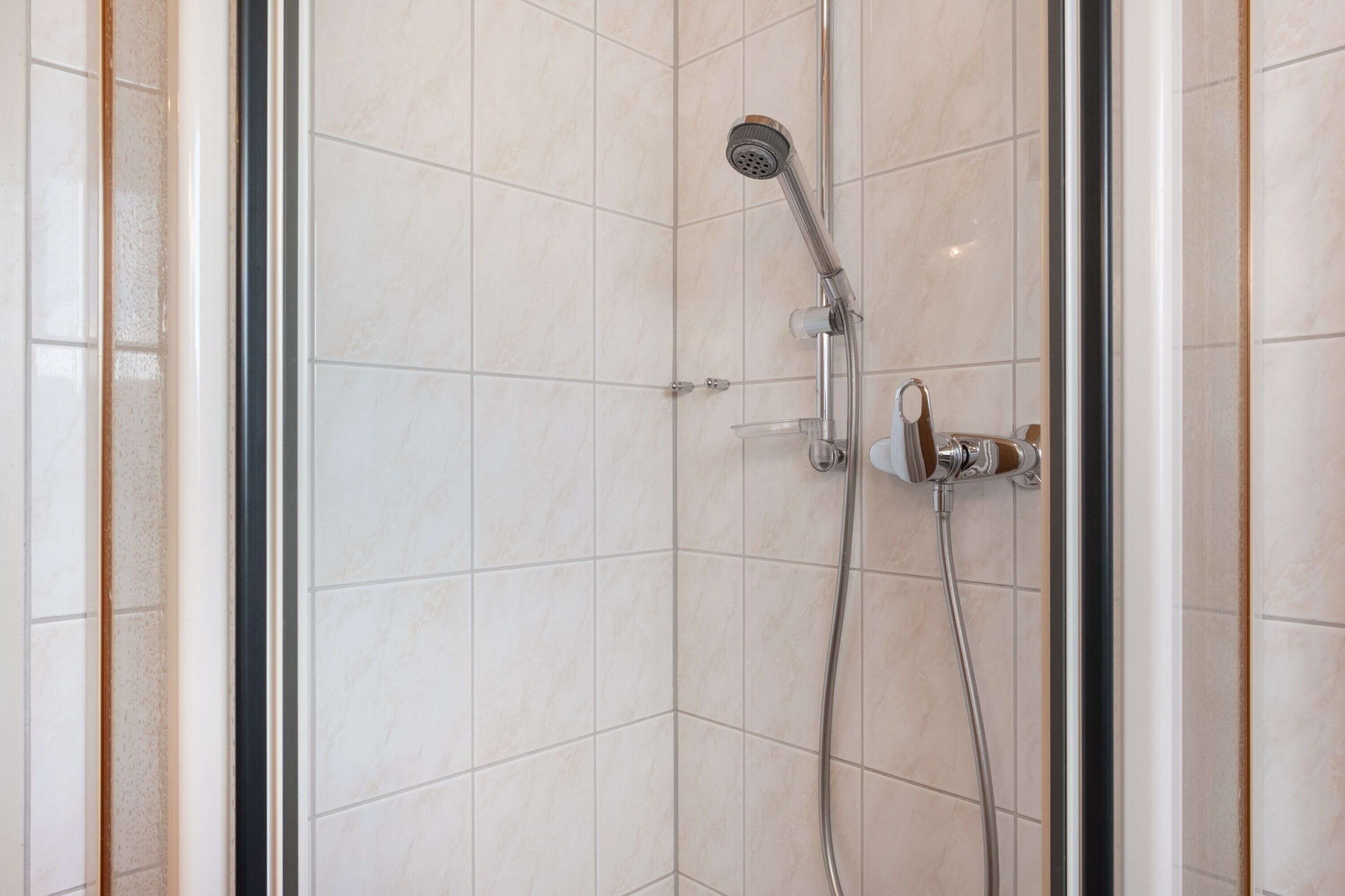 A glass-enclosed shower with a handheld showerhead and a wall-mounted faucet.