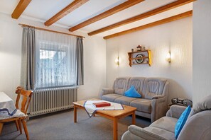 Una sala de estar con un sofá, una mesa con un libro, un radiador y una ventana con cortinas.