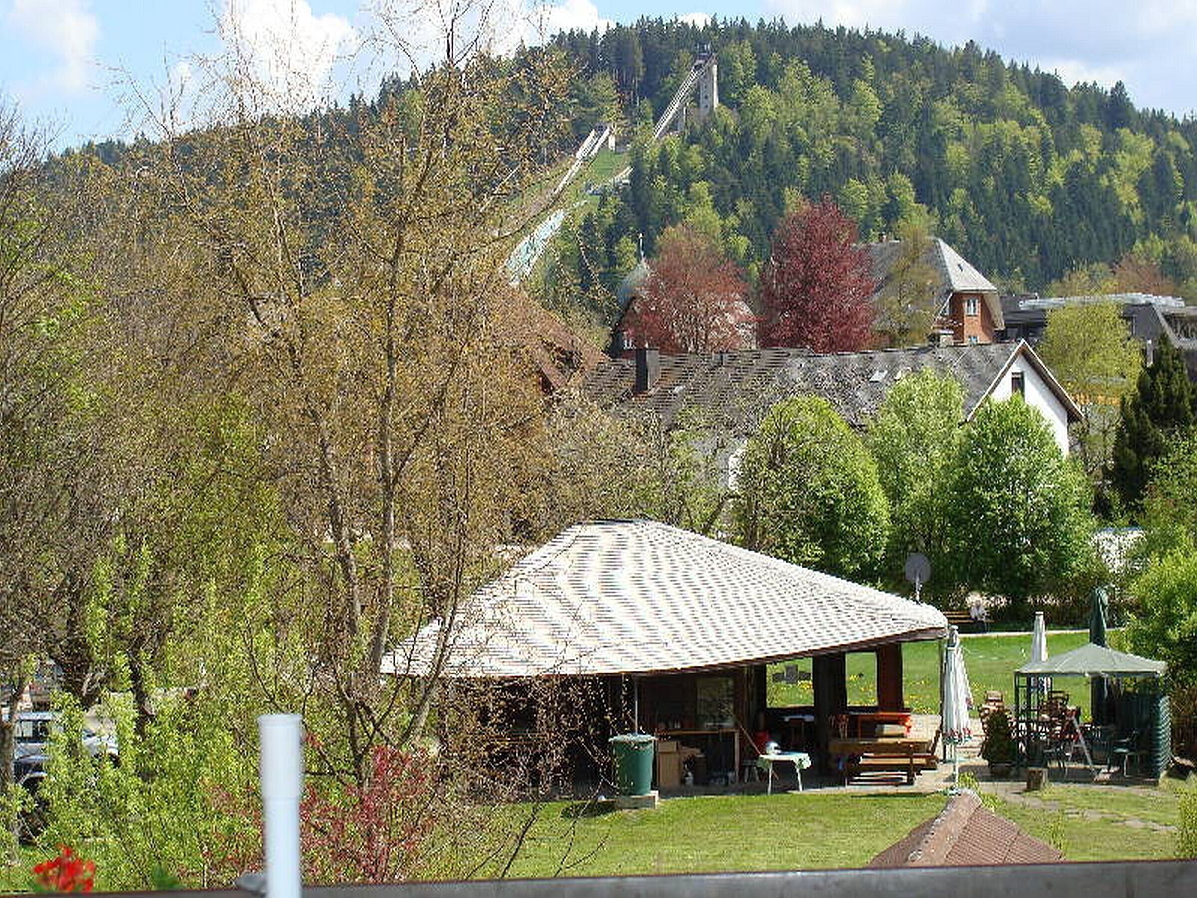 Ländliche Szenerie mit einem Gebäude mit Schrägdach, einer überdachten Sitzgelegenheit und Bergblick.