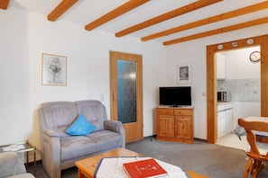 Una sala de estar con un sofá, un televisor, un mueble de madera y una zona de comedor con una mesa y una silla.