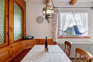 Un coin repas comprenant une table, des chaises, une bouteille de vin, une horloge et une fenêtre avec des rideaux.