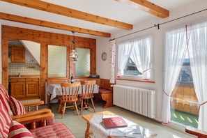 Une pièce chaleureuse avec des poutres apparentes, une table à manger avec des chaises, un canapé et une vue par la fenêtre.