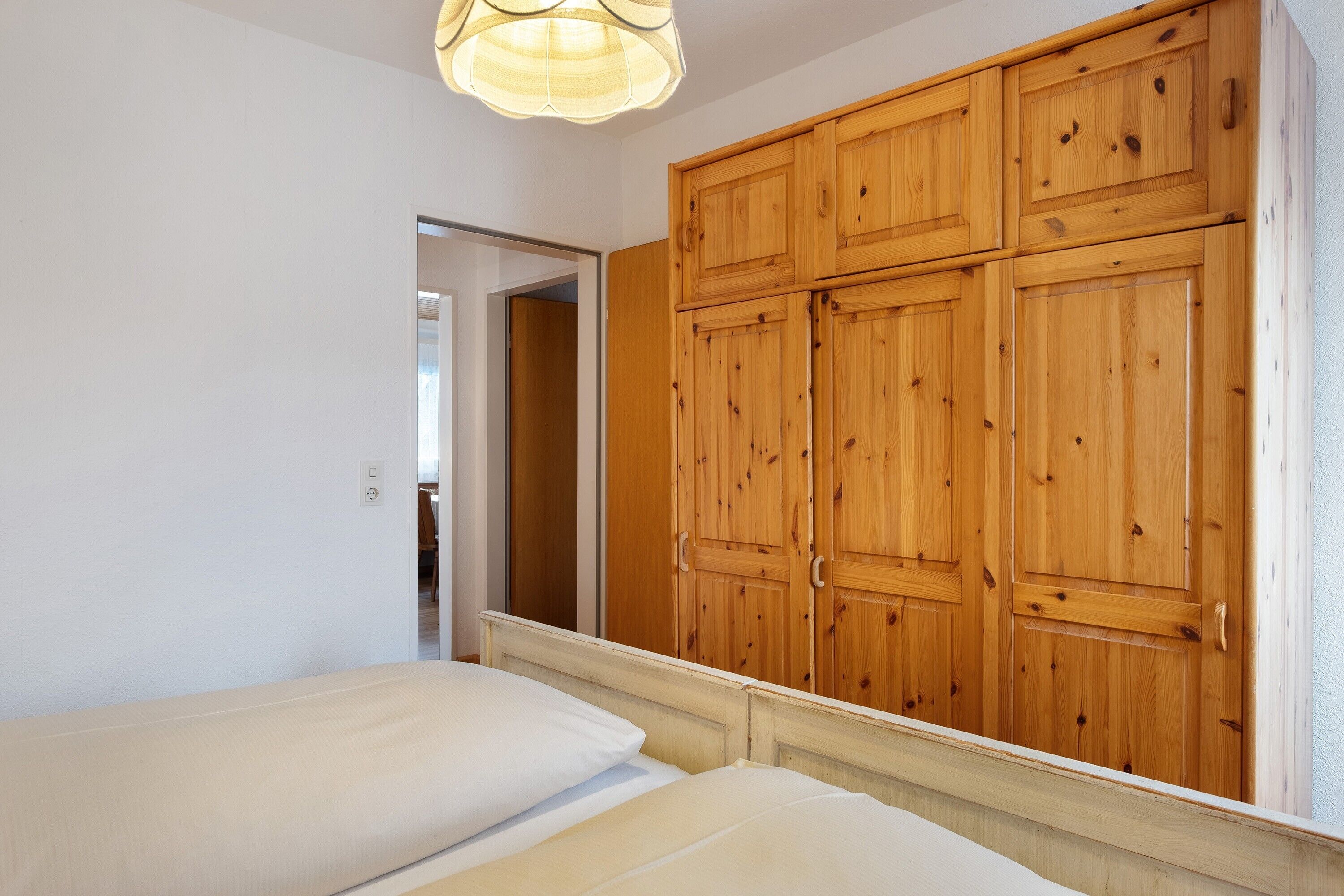 A bedroom with a wooden wardrobe, a bed with white bedding, and a light fixture above the bed.