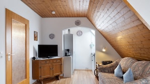 A room with a wooden ceiling, a television on a wooden cabinet, a sofa with cushions, and a door with a textured panel. - Holiday Apartment '2' with Mountain View, Shared Garden and Wi-Fi (Hinterzarten)