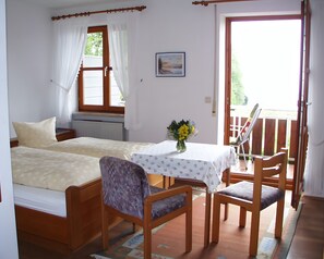 Ein Zimmer mit zwei Betten, einem Tisch mit Blumenvase und einem Balkon mit Stühlen.