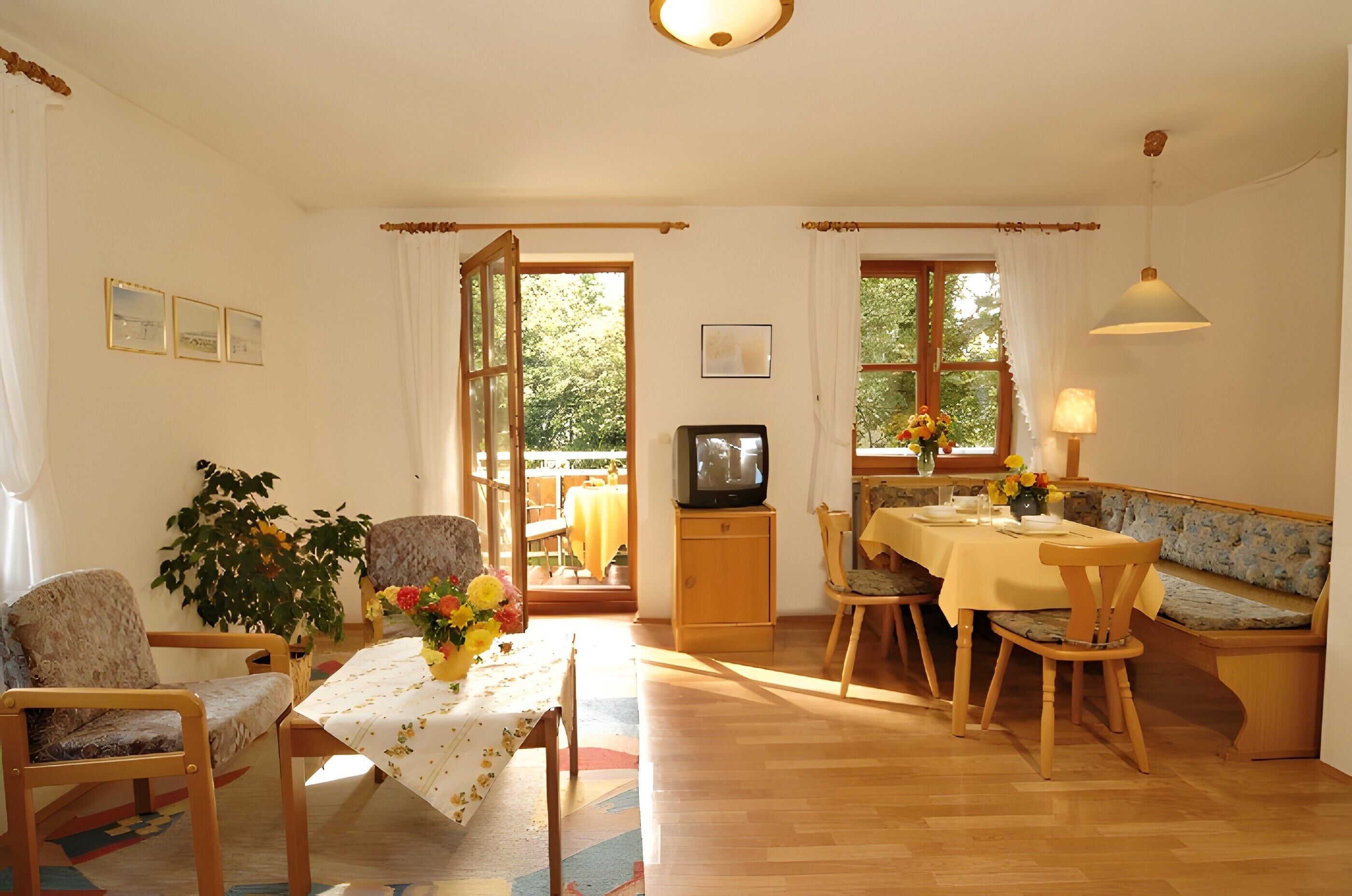 Ein Essbereich mit einem Tisch für vier Personen, Stühlen, einer Bank, einem Fernseher und einem fenster mit Vorhängen.