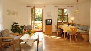 A dining area with a table set for four, chairs, a bench, a television, and a window with curtains.