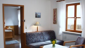 A room with a sofa, a table with a vase, a chair, a bed, a window with curtains, and a radiator.