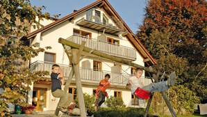 A residential building with a balcony, a wooden swing set, and a grassy yard.