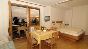 Une pièce comprenant un lit, une table à manger avec des chaises, un téléviseur et une fenêtre avec des rideaux.