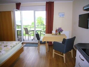 A room with a bed, a table with chairs, a TV, and a balcony with a view.
