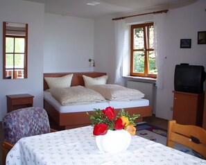 A bedroom with a bed, a bedside table, a chair, a TV, and a window with curtains.