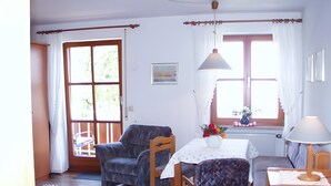 Une pièce avec une chaise en bois, une table ornée d’un vase de fleurs, une fenêtre avec des rideaux et une lampe.