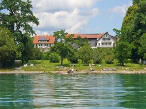 Une vue sur le lac, avec une maison dotée d’un toit rouge et de panneaux solaires, entourée de verdure et d’arbres.