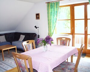 Una sala de estar con un sofá, una mesa de comedor con sillas, un jarrón con flores y una ventana con cortinas.