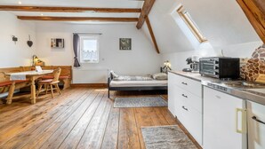Une chambre confortable située dans les combles, avec un plafond en bois, un lit, une petite kitchenette et un coin repas comprenant une table et des chaises.