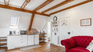 Une cuisine avec des poutres en bois, un canapé rouge et une horloge au mur.