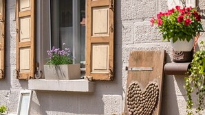Fachada de edificio con ventana, persianas de madera, una decoración con forma de corazón y una maceta con flores.
